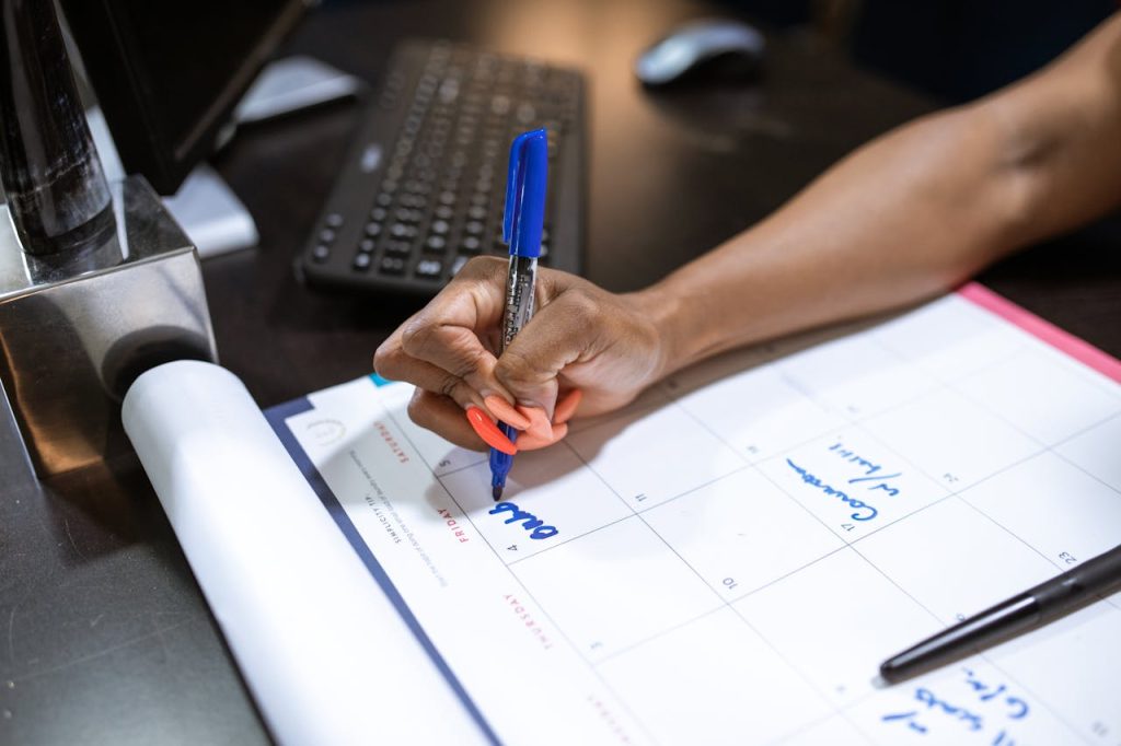 Detailed shot of a persons hand writing notes on a calendar using a blue marker.